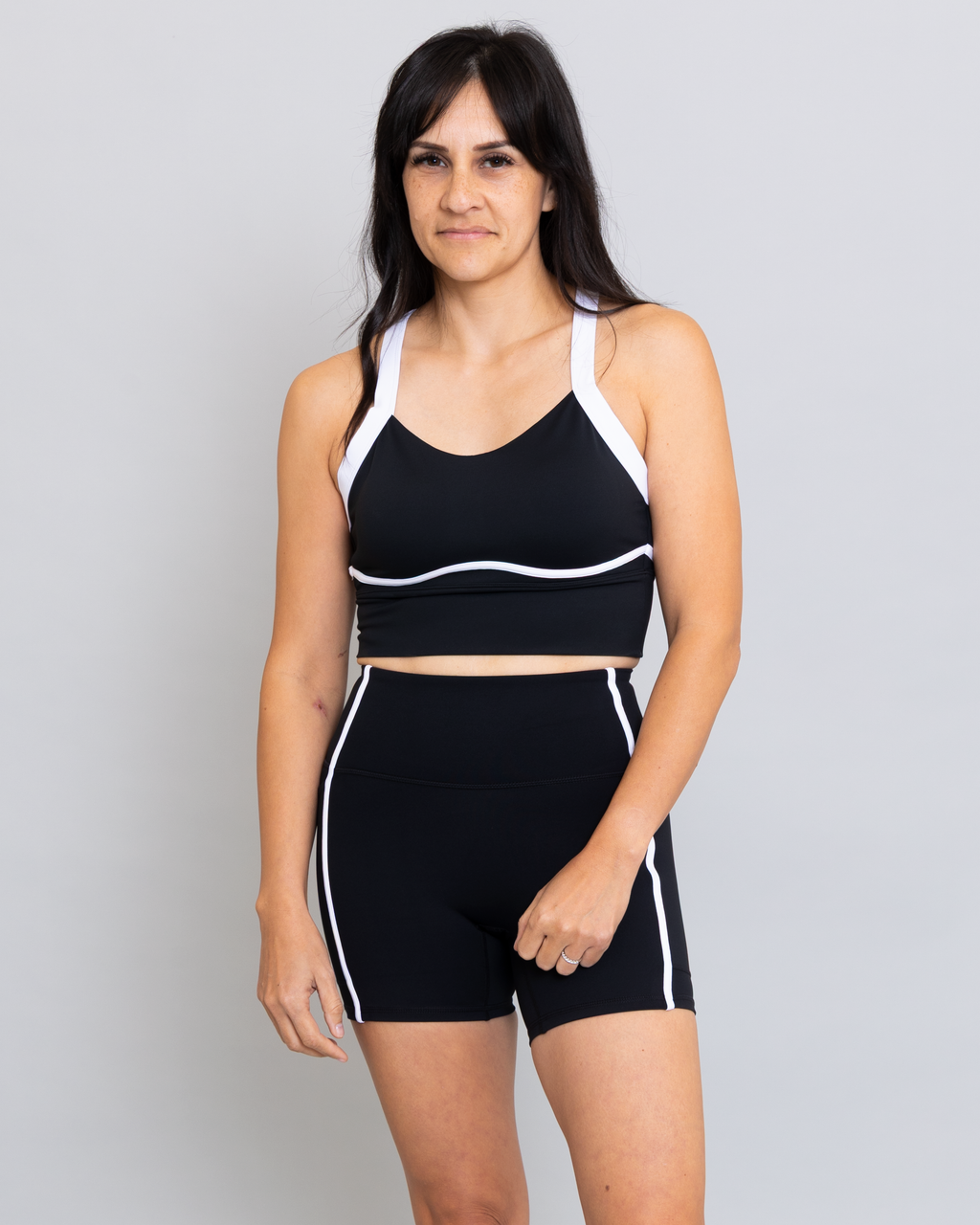 Woman wearing a black sports bra and shorts with white accents on a gray background