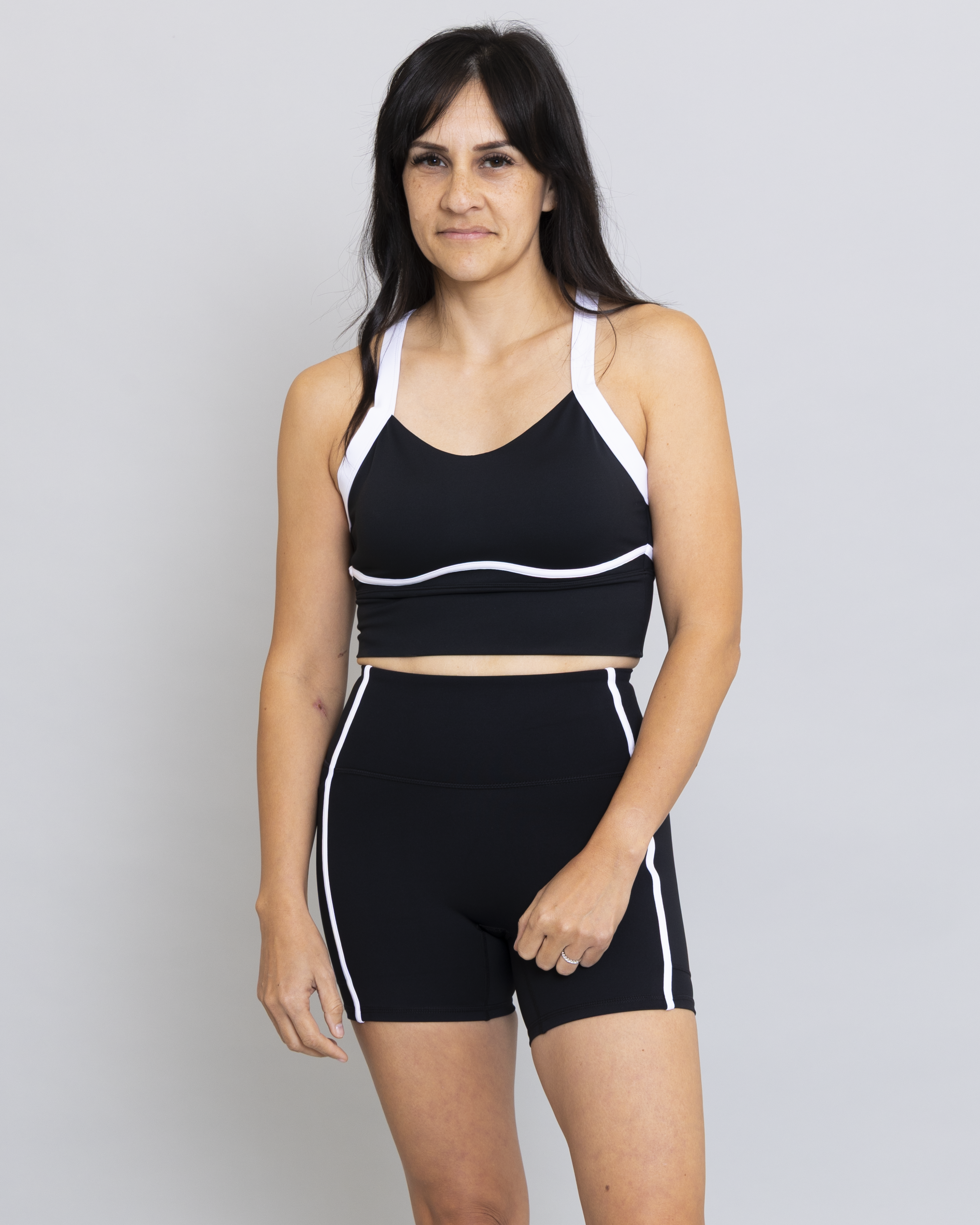 Woman wearing a black sports bra and shorts with white accents on a gray background