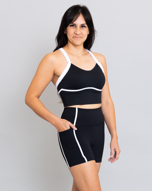 Woman wearing a black sports bra and shorts with white trim on a gray background