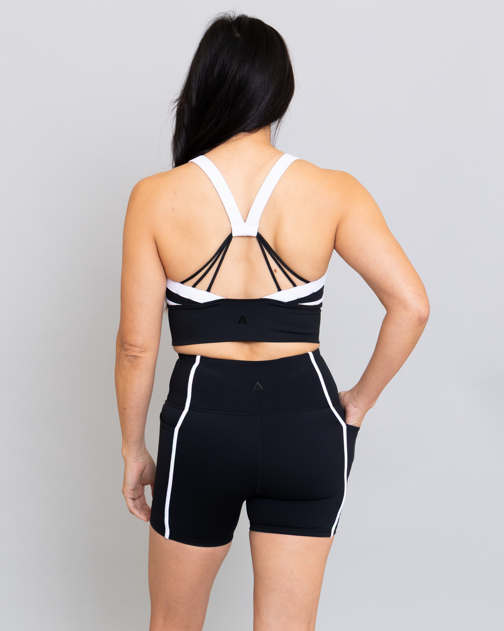 Person wearing a black sports bra and shorts with white accents on a gray background