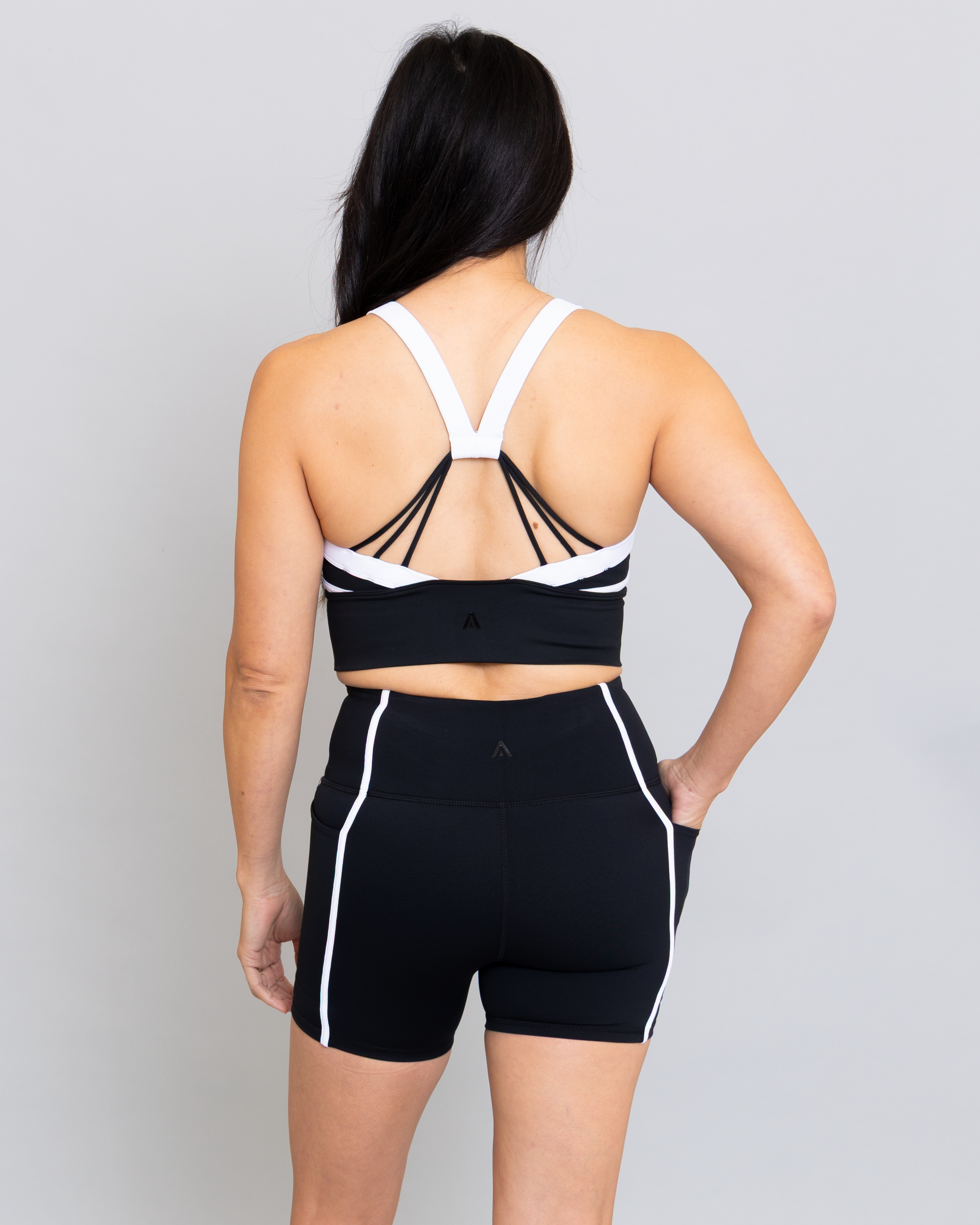 Person wearing a black sports bra and shorts with white accents on a gray background