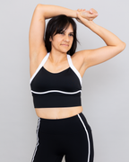 Woman wearing a black sports bra and leggings with white accents against a gray background