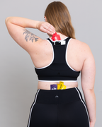 Person wearing a black sports bra and leggings with visible tattoos on a gray background