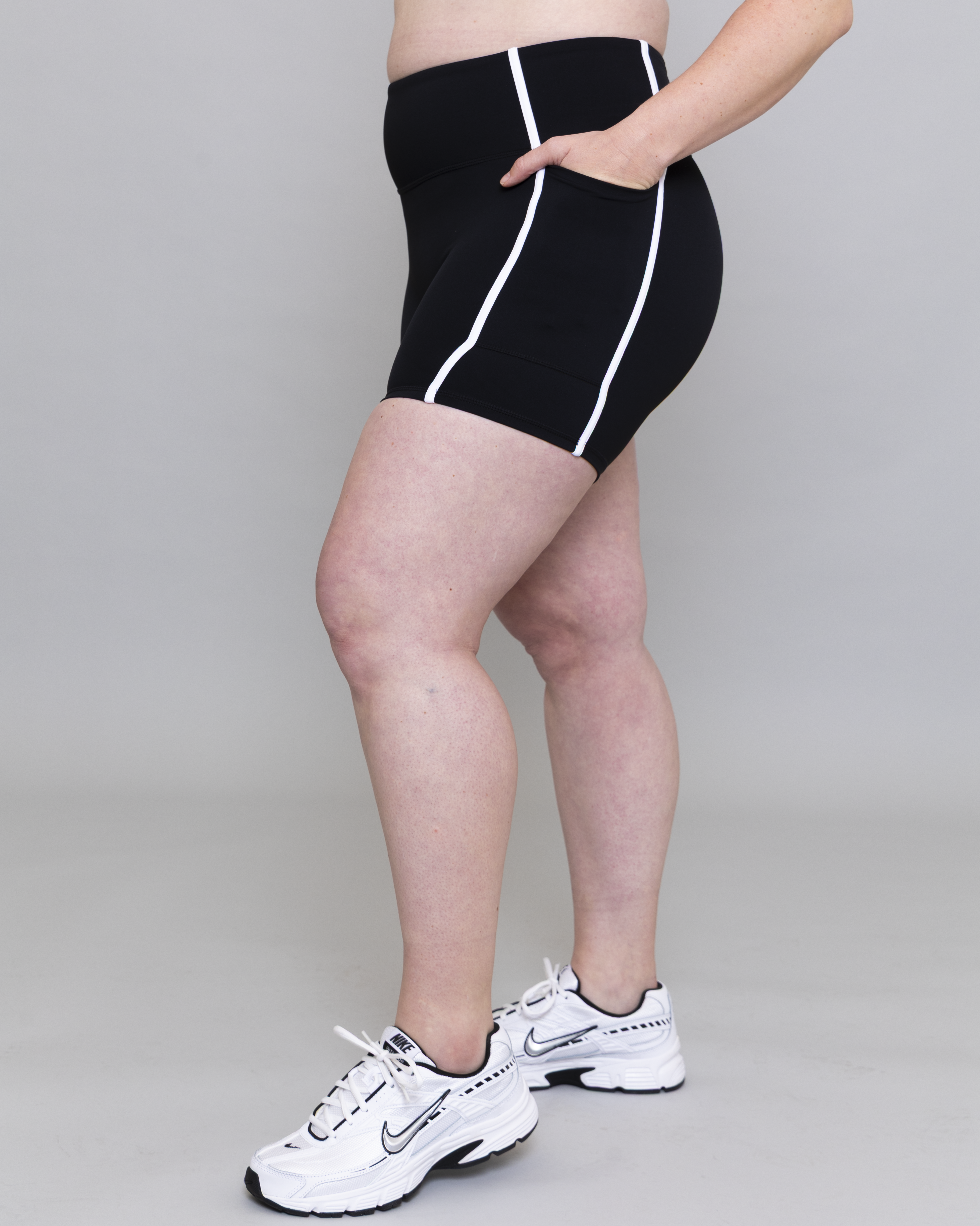 Person wearing black shorts with white stripes and white sneakers on a gray background