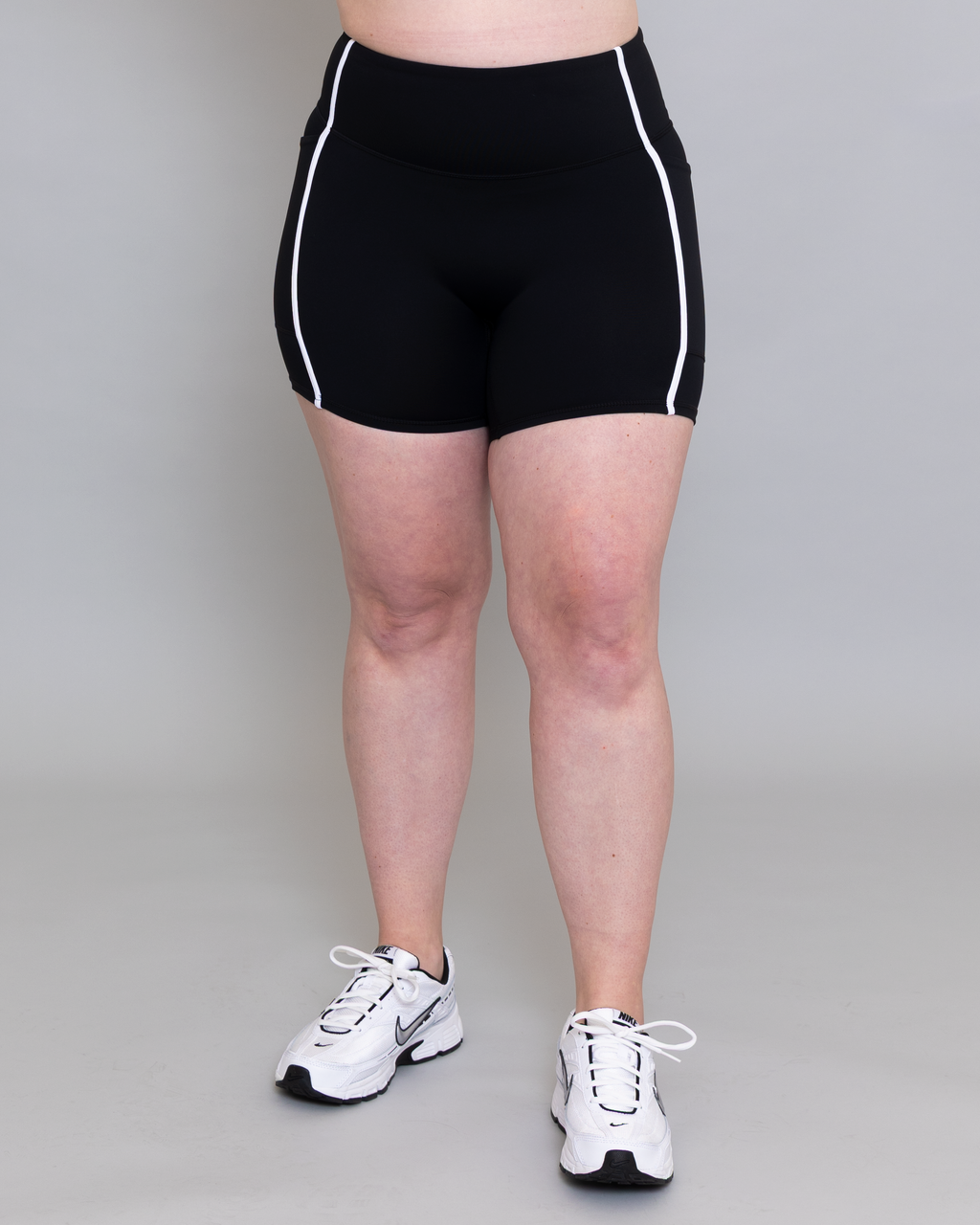 Person wearing black athletic shorts with white trim on a plain background