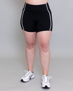 Person wearing black athletic shorts with white trim on a plain background