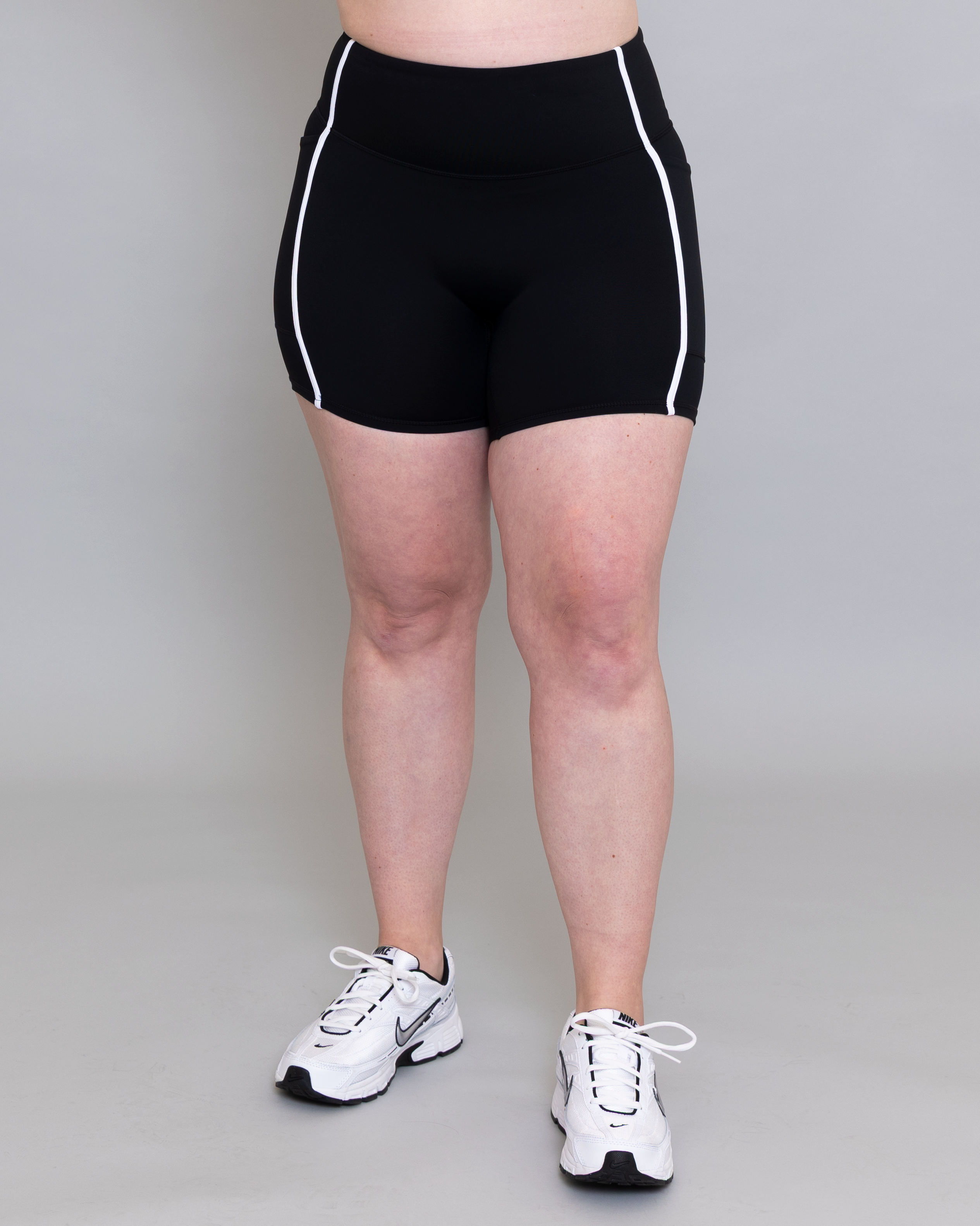 Person wearing black athletic shorts with white trim on a plain background