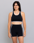 Woman wearing a black sports bra and shorts with white stripes on a gray background