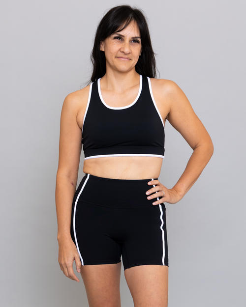 Woman wearing a black sports bra and shorts with white trim on a gray background