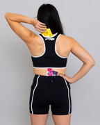 Person wearing a black sports bra and shorts set with visible branding on a gray background