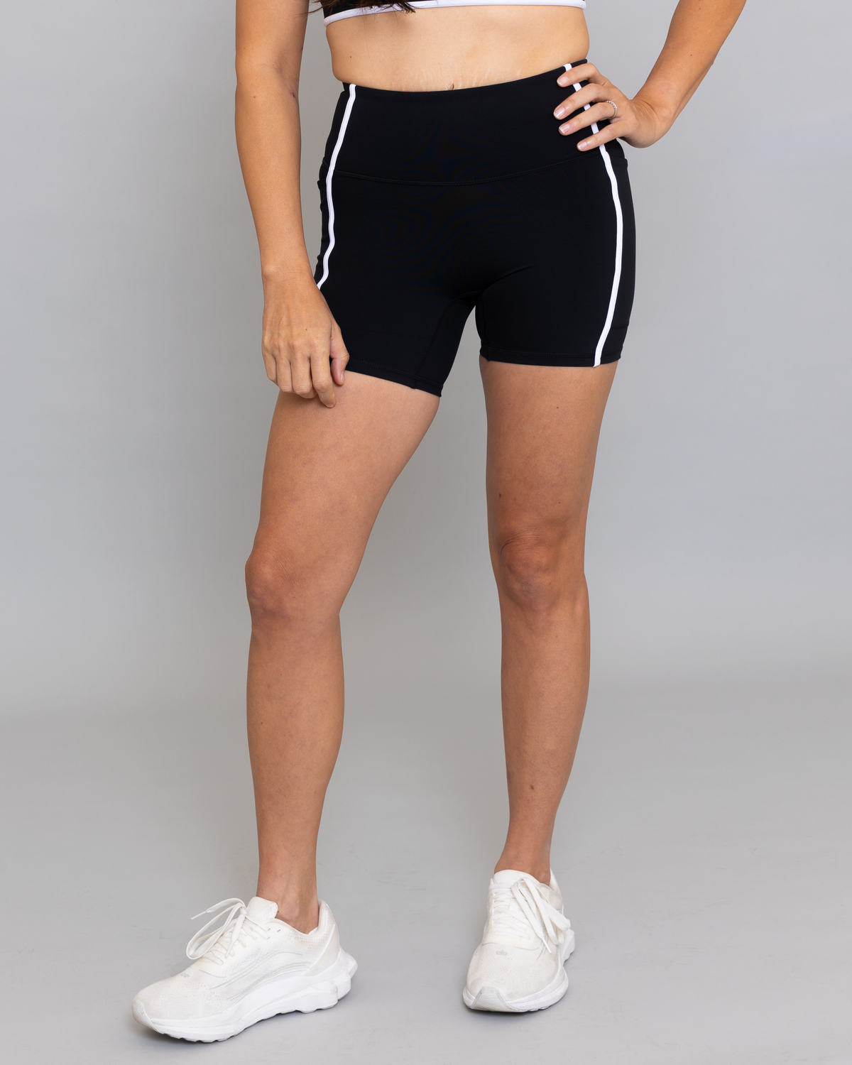 Person wearing black athletic shorts with white stripes on a gray background
