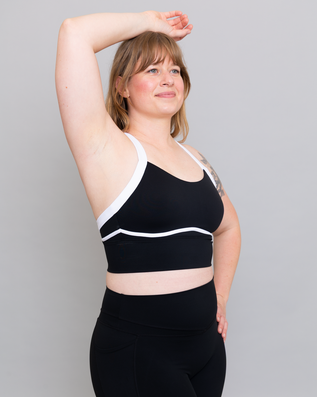 Woman wearing a black sports bra with white accents against a gray background