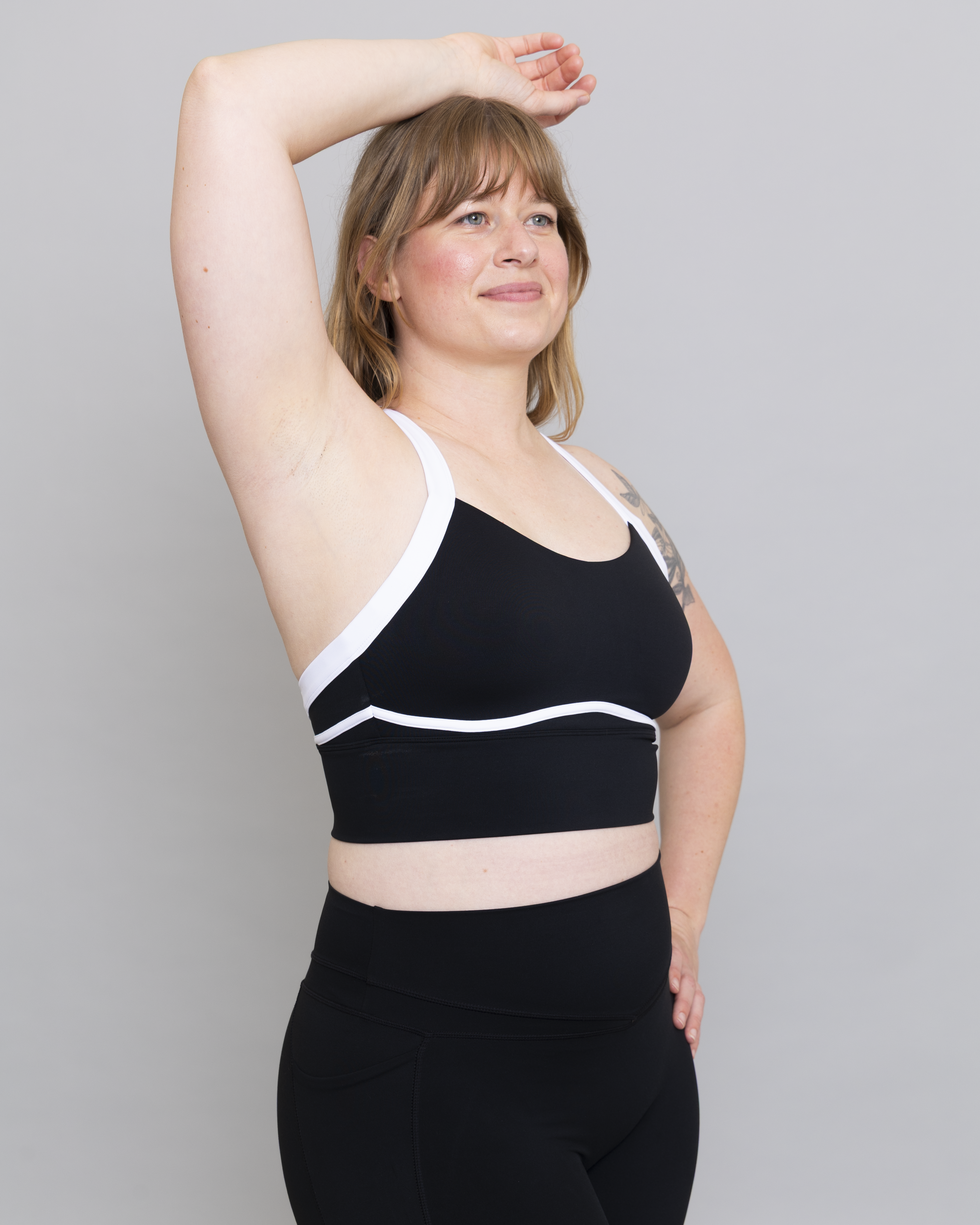 Woman wearing a black sports bra with white accents against a gray background