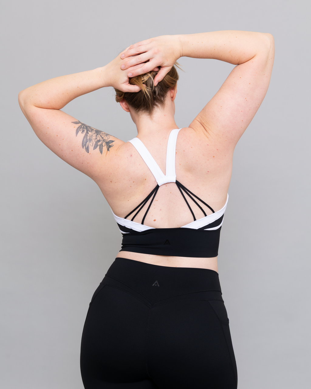 Person wearing a black and white sports bra with strappy details on a gray background