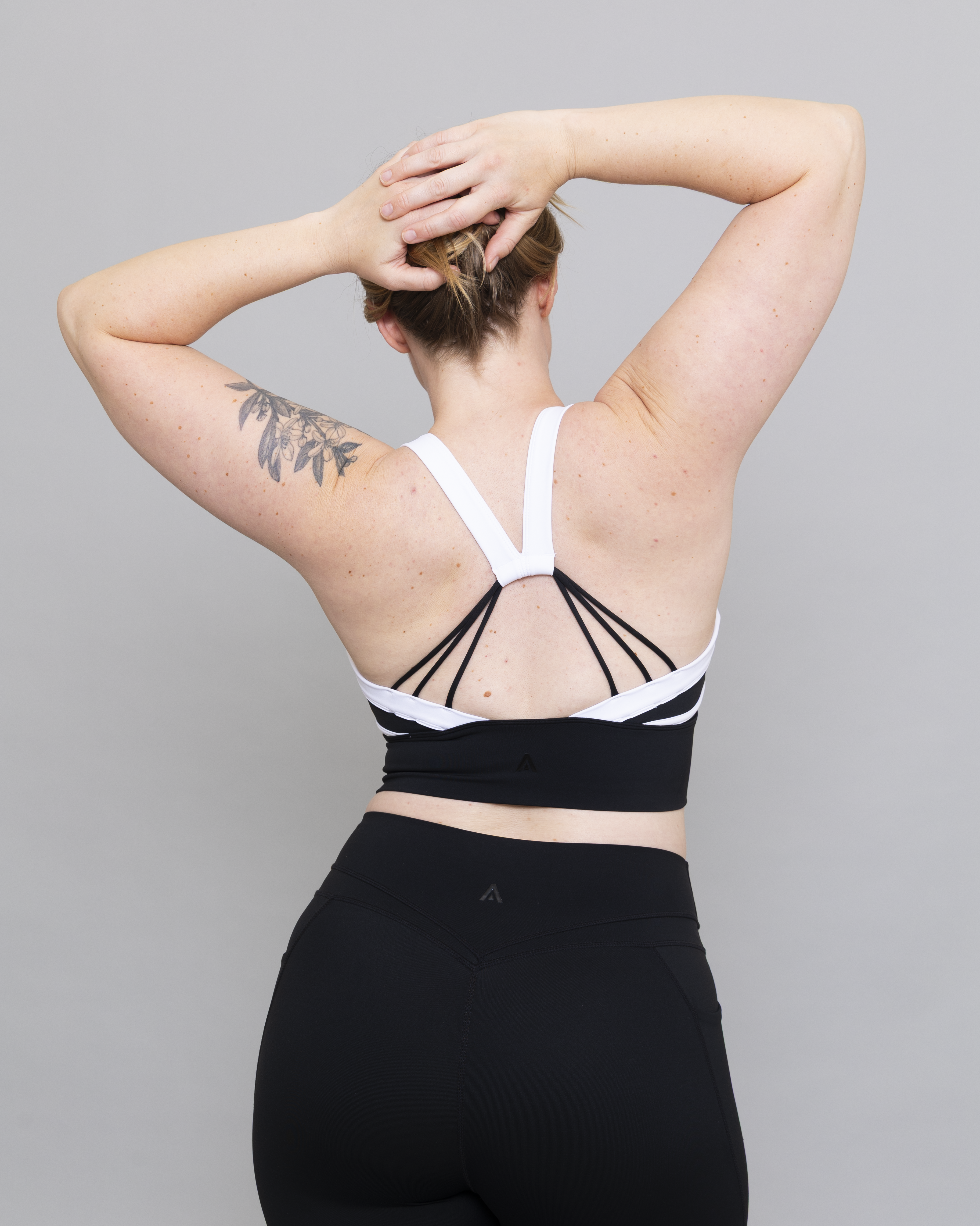 Person wearing a black and white sports bra with strappy details on a gray background
