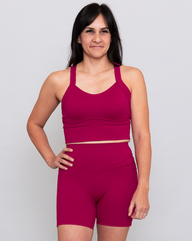 Woman wearing a magenta sports bra and shorts set on a plain background
