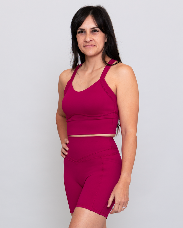 Woman wearing a magenta sports bra and shorts on a white background