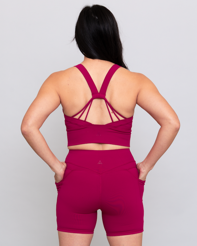 Person wearing a magenta sports bra and shorts set on a light gray background