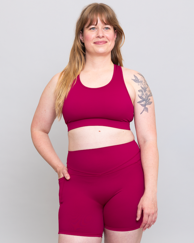 Woman wearing a magenta sports bra and shorts set on a plain background