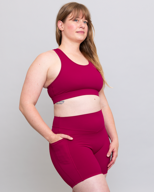 Woman wearing a magenta sports bra and shorts set on a plain background