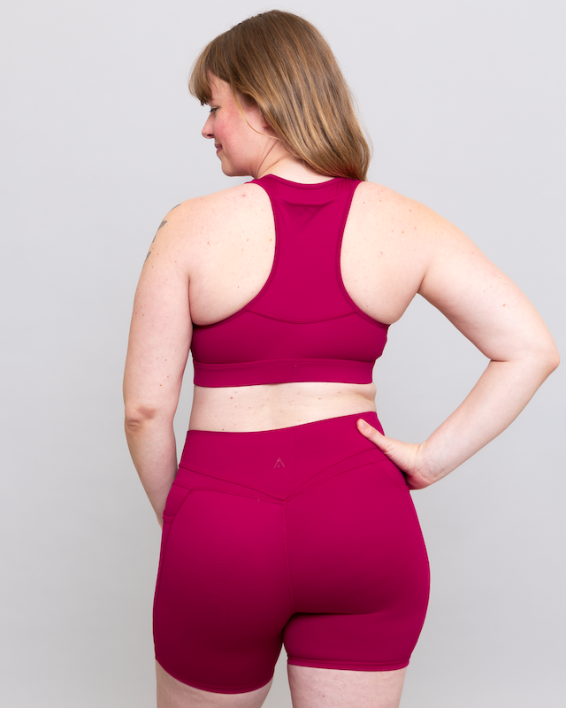 Woman wearing a magenta sports bra and shorts set on a plain background