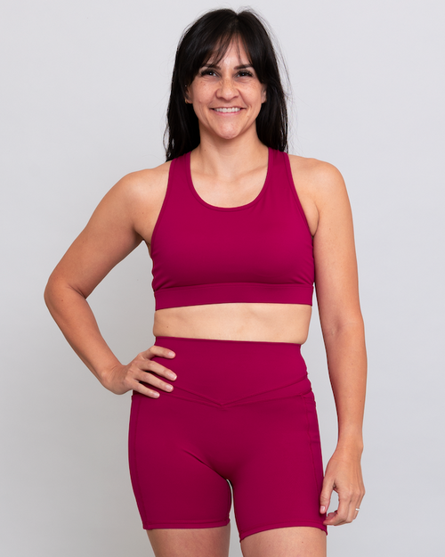 Woman wearing a magenta sports bra and shorts set on a light gray background