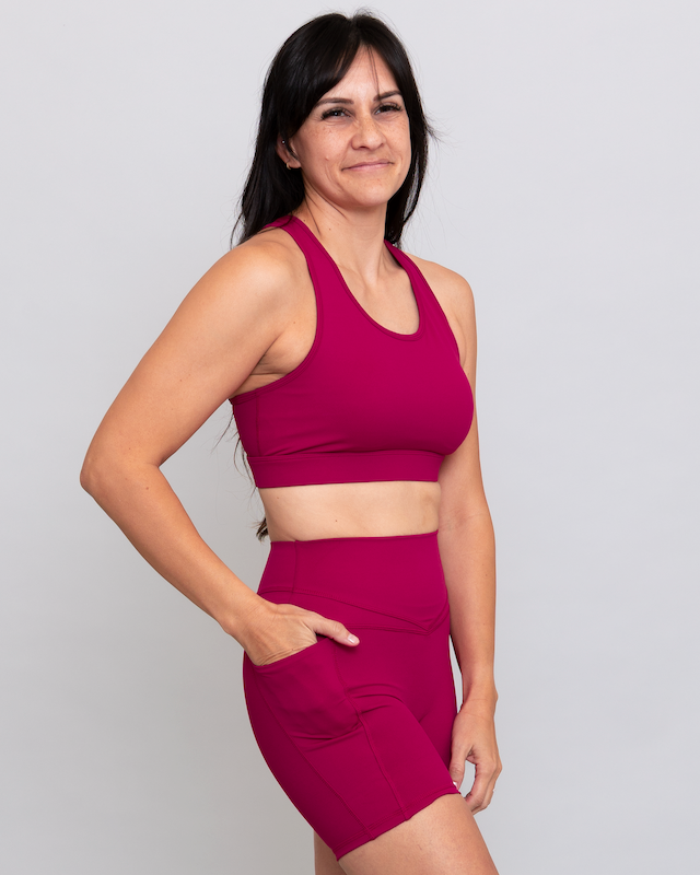 Woman wearing a magenta sports bra and shorts set on a plain background