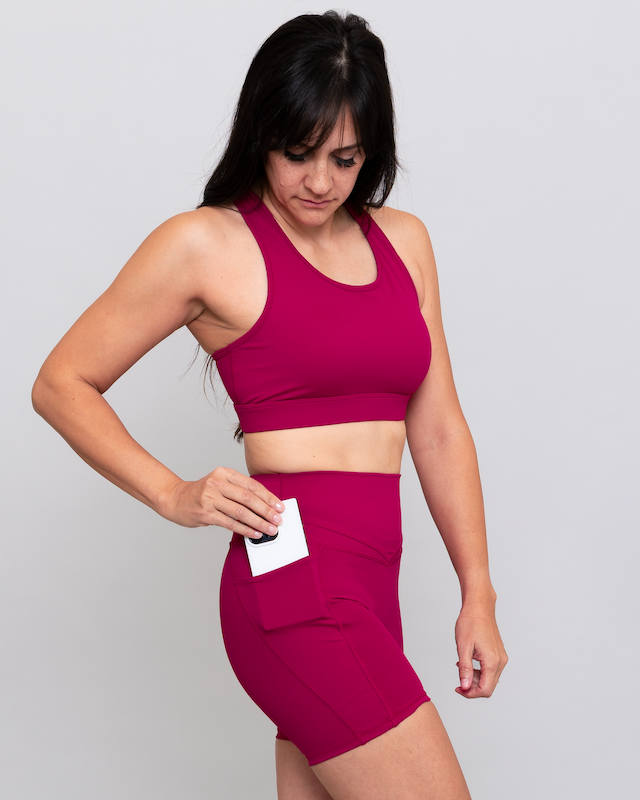 Woman wearing a magenta athletic outfit holding a white card against a gray background