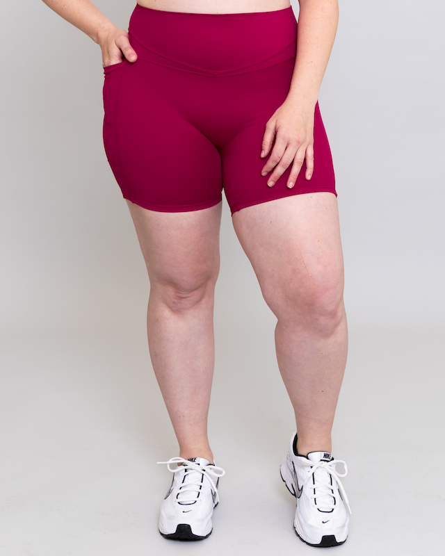 Person wearing magenta athletic shorts and white sneakers on a plain background