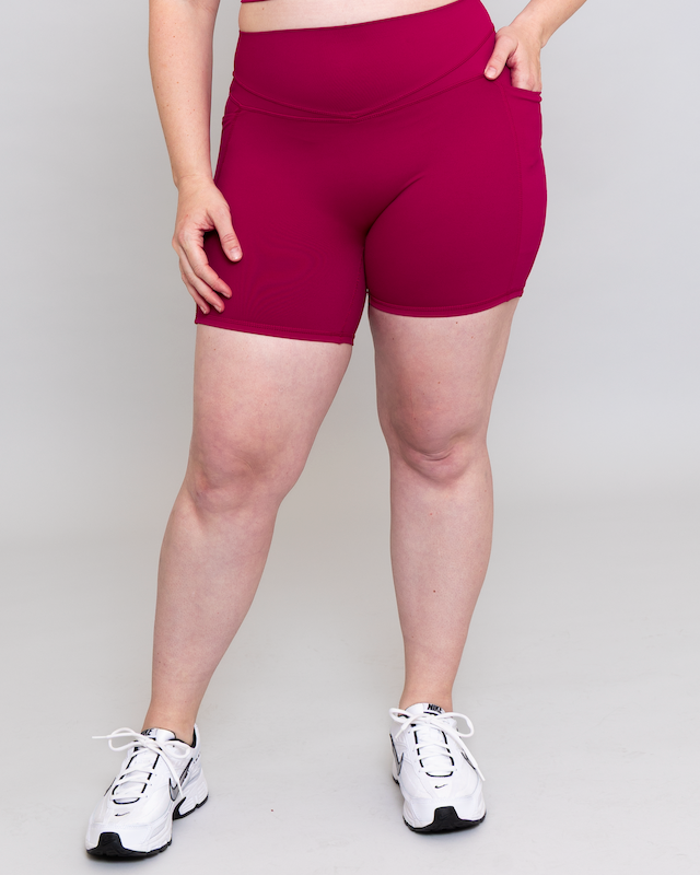 Person wearing magenta shorts and white sneakers on a plain background