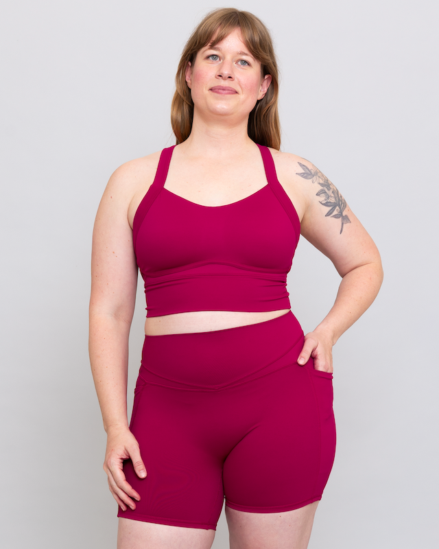 Woman wearing a magenta sports bra and shorts set on a plain background