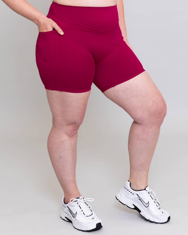 Person wearing magenta shorts and white sneakers on a plain background