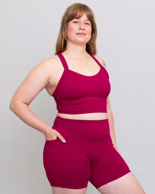 Woman wearing a magenta sports bra and shorts set on a plain background