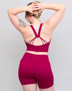 Person wearing a magenta sports bra and shorts set on a gray background