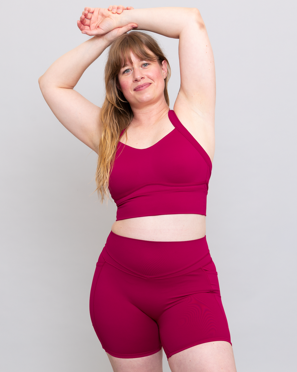 Woman wearing a magenta sports bra and shorts set on a light gray background