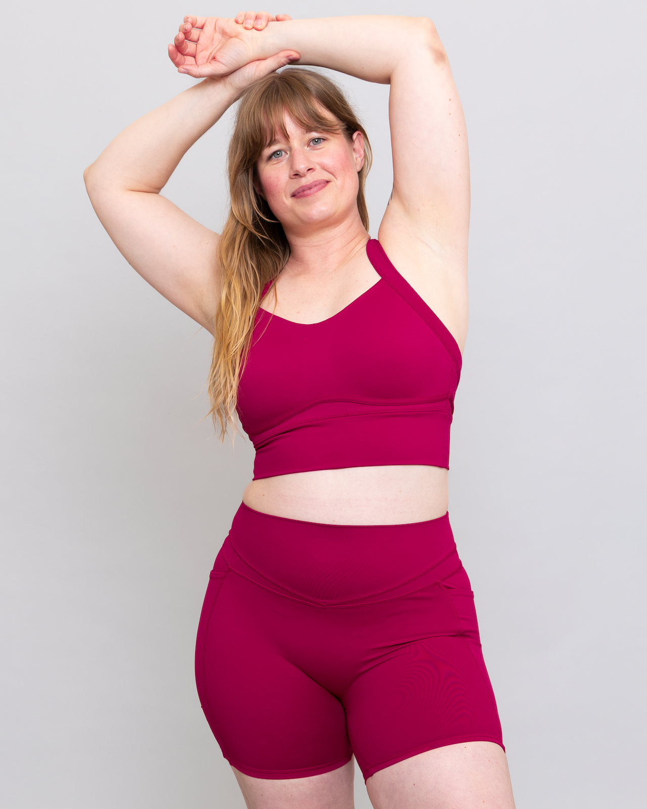 Woman wearing a magenta sports bra and shorts set on a light gray background