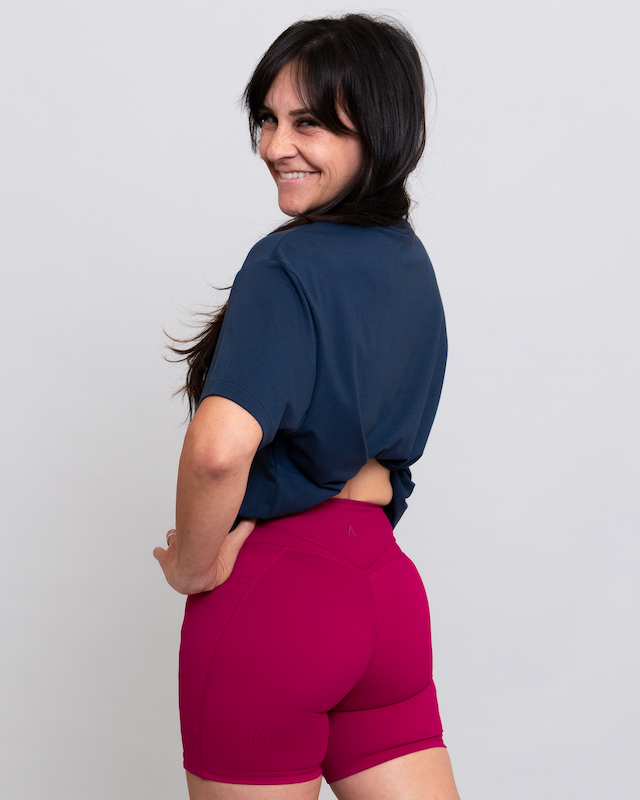 Woman wearing a navy blue top and pink shorts on a light gray background