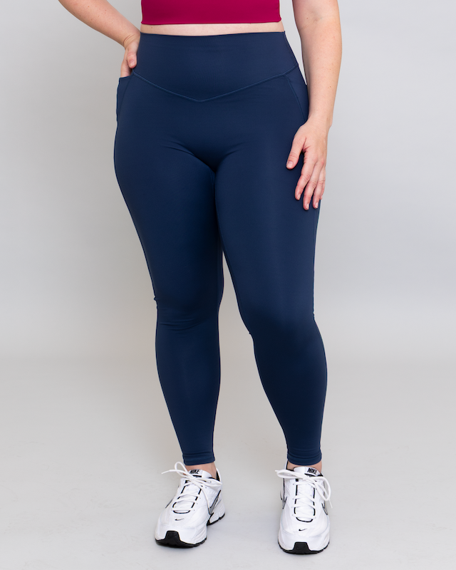 Person wearing navy leggings and white sneakers on a plain background