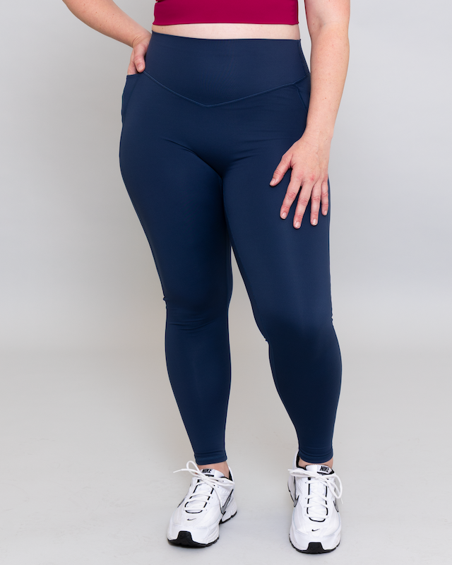 Person wearing navy leggings and white sneakers on a plain background