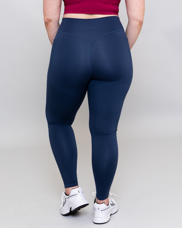 Person wearing navy leggings and white sneakers on a plain background
