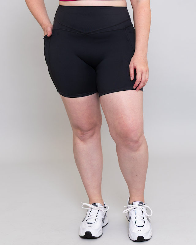Person wearing black athletic shorts and white sneakers on a plain background