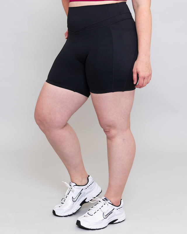 Person wearing black athletic shorts and white sneakers on a plain background