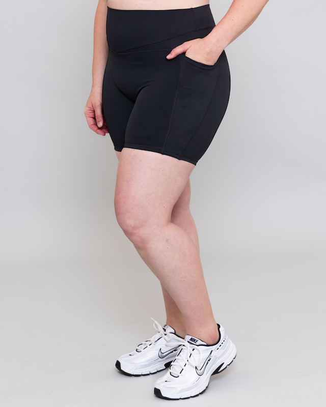 Person wearing black athletic shorts and white sneakers on a plain background